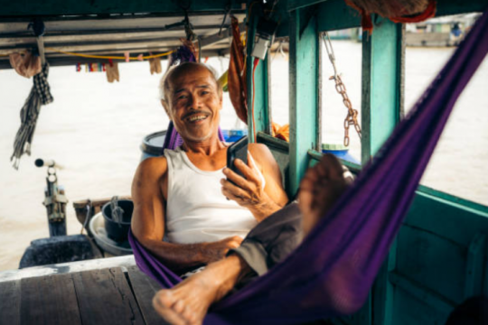 Homme se relaxant dans un hamac à bord de son bateau sur le delta du Mékong © Nikada